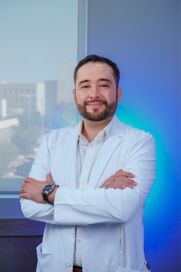 Dr. Erick Alvidrez con bata médica, de brazos cruzados, en su consultorio